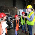 A group of children in hard hats standing in a warehouse.