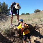 A woman with a backpack is helping a boy to dig a hole.