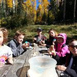 A group of kids eating at a picnic table in the woods.