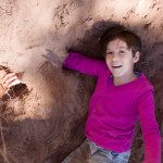 A girl in a pink shirt is playing in a sand pit.
