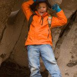 A boy in an orange jacket standing in a cave.