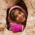 A girl peeking out of a hole in a rock.