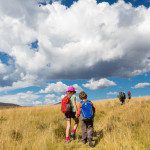 children hiking in grassy area with big clouds