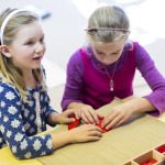 two children folding red felt on a table