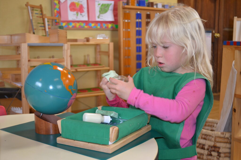 child playing with items from a wooden green felt box